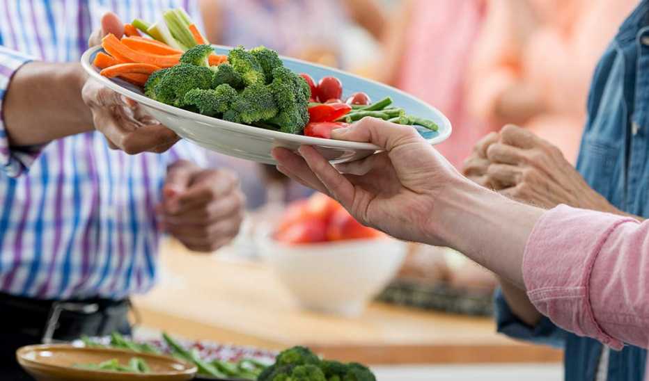 A person handing another person a plate of vegetables