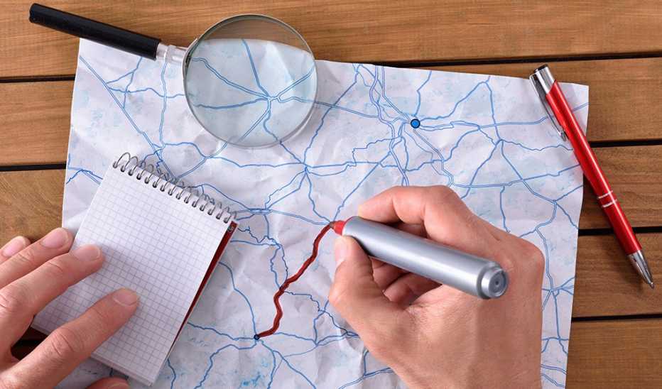 A hand traces a path on a map that lies on a wooden table