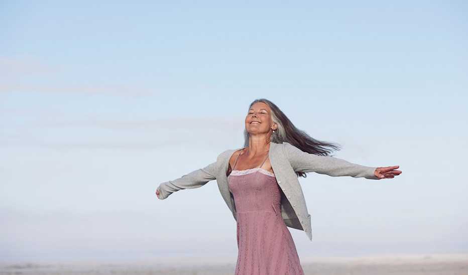 A smiling woman with her arms raised on a beach