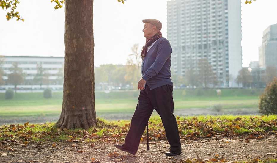 A man walking with a cane in a park in a city