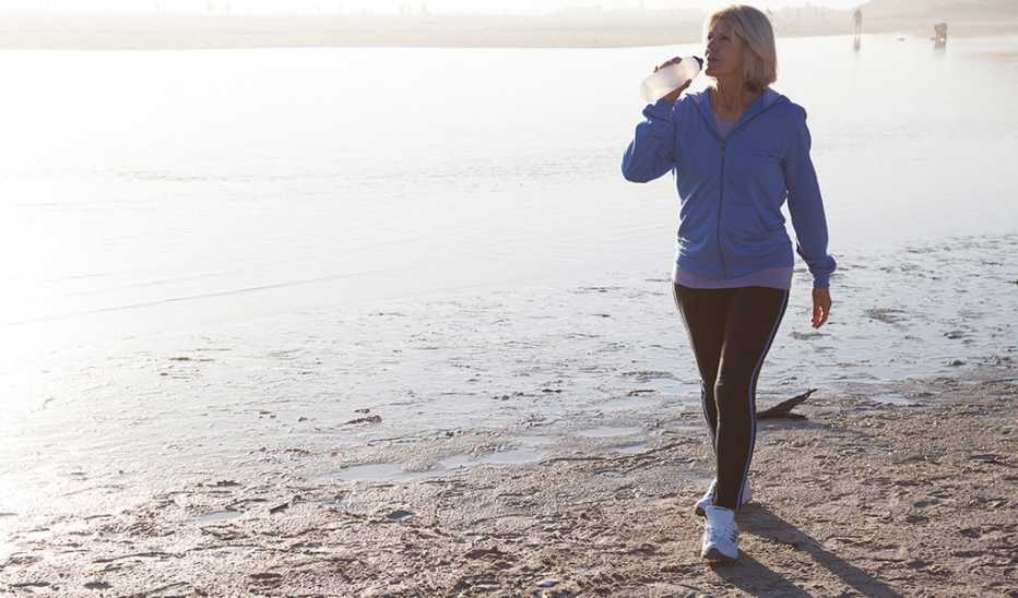 A woman drinking water as she takes a walk on the beach