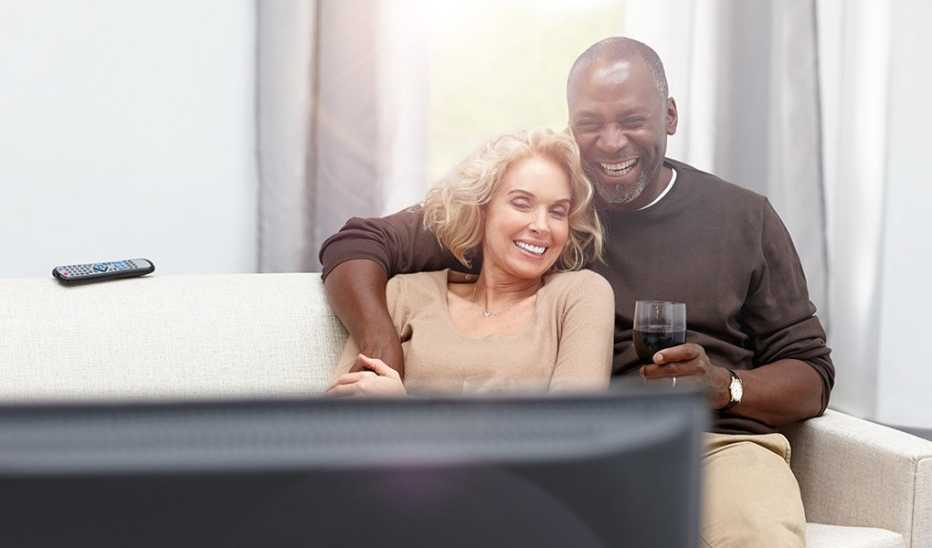 A couple cuddling on the couch together as they watch TV and drink wine