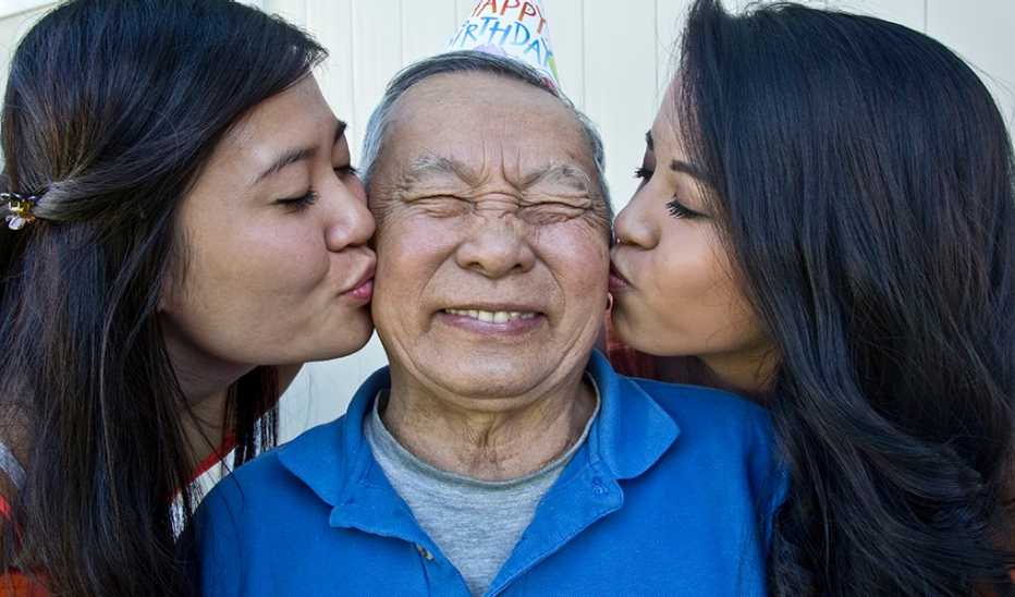 Two younger women kissing an older man on both cheeks on his birthday