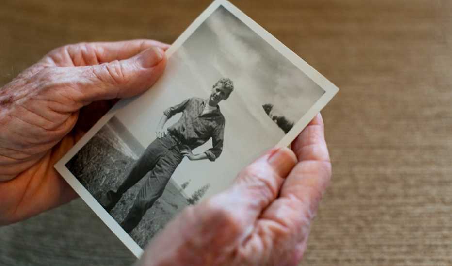 A close up of older hands holding an old photo of a young man