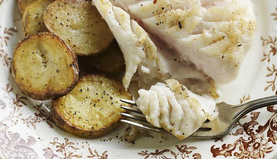 A close-up view of a fillet of cod with pan roasted potatoes on a plate