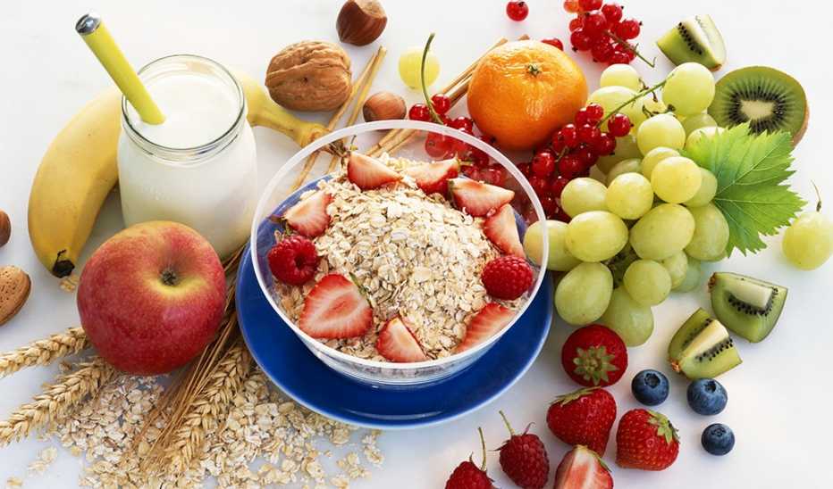 A close-up view of a bowl of muesli surrounded by fruits and a glass of milk