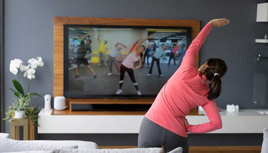 Back view of a woman stretching as she watches an exercise class on TV