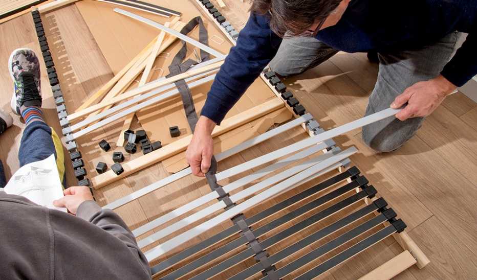 Two men assembling a bed with lots of parts scattered on the floor