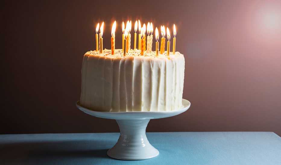 A white birthday cake with candles on a stand against a dark background