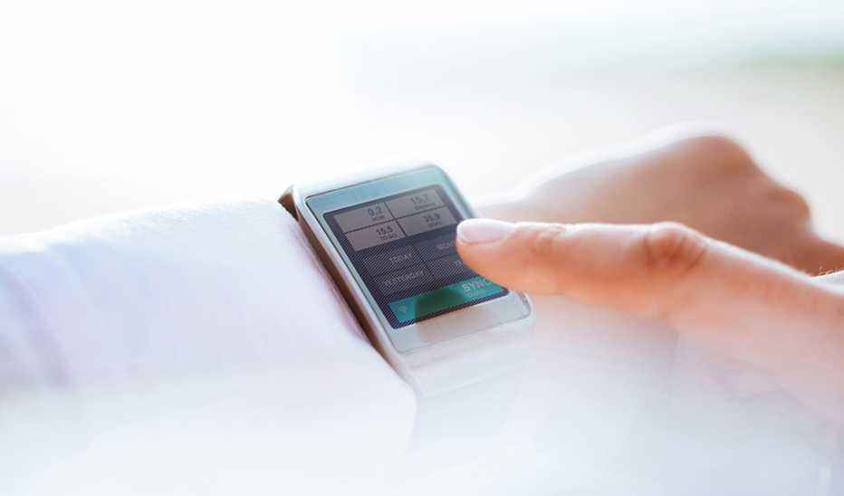 A finger pointing at a smartwatch on a person’s wrist