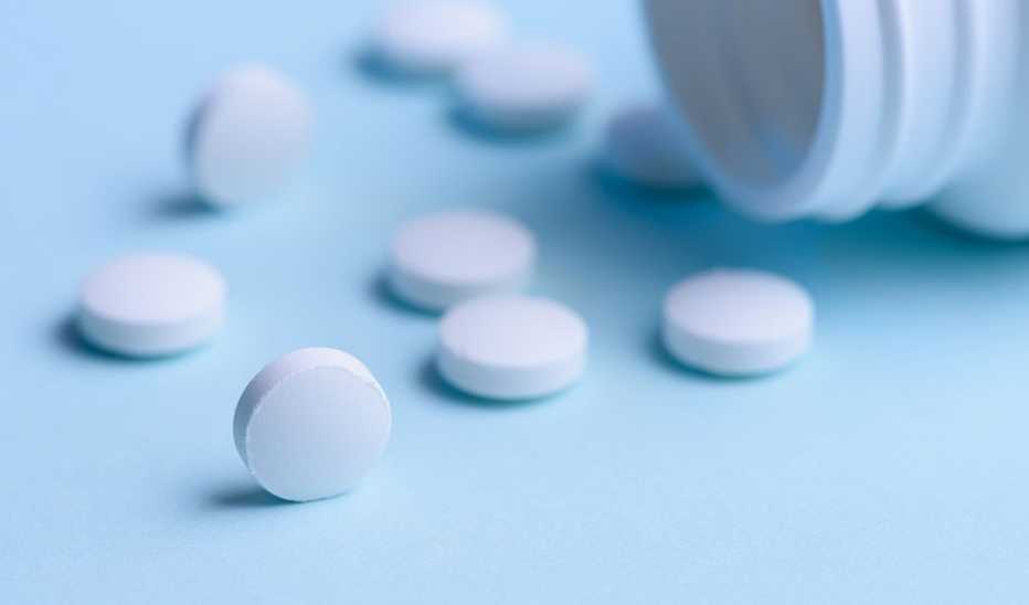 A close-up view of white pills and bottle on a blue background