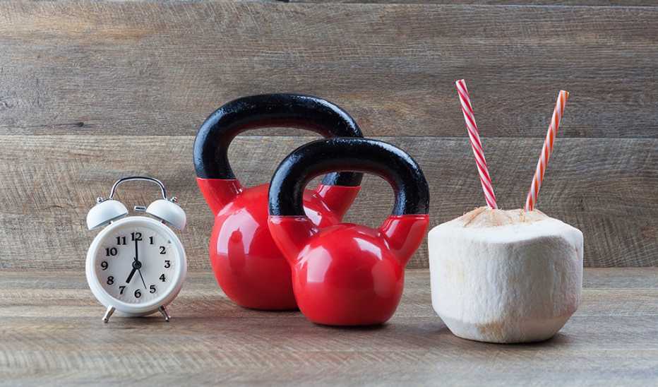 Two kettlebells with a drinking coconut and clock on a wooden table