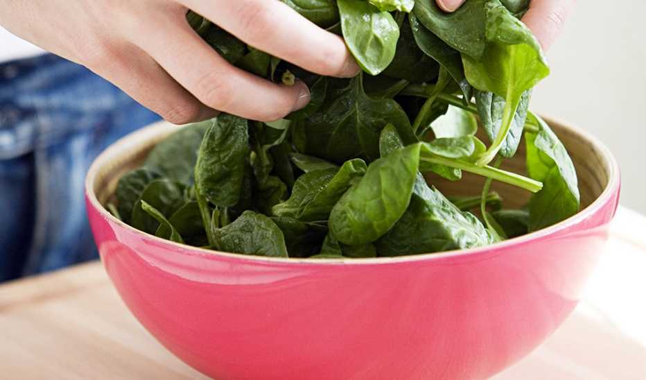 A person preparing spinach in a bowl