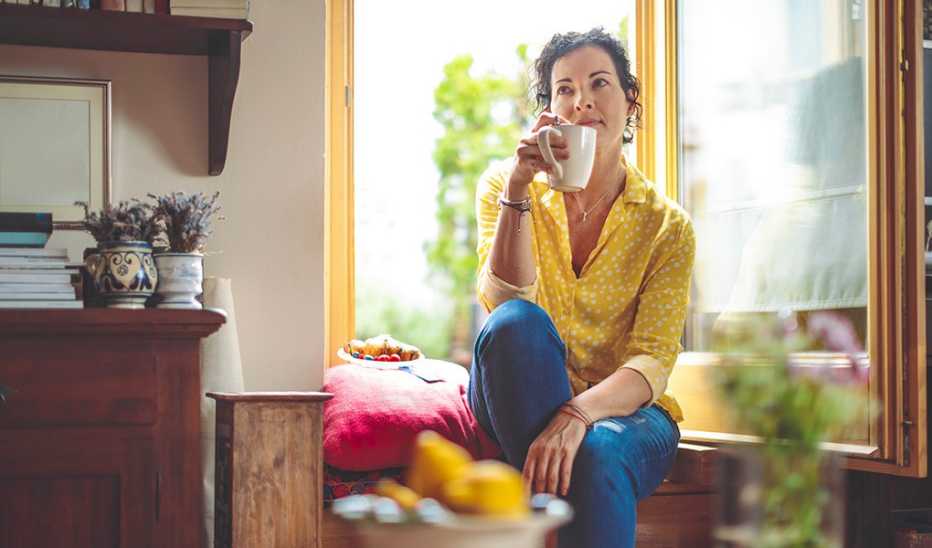 A woman is sitting and drinking a coffee at home