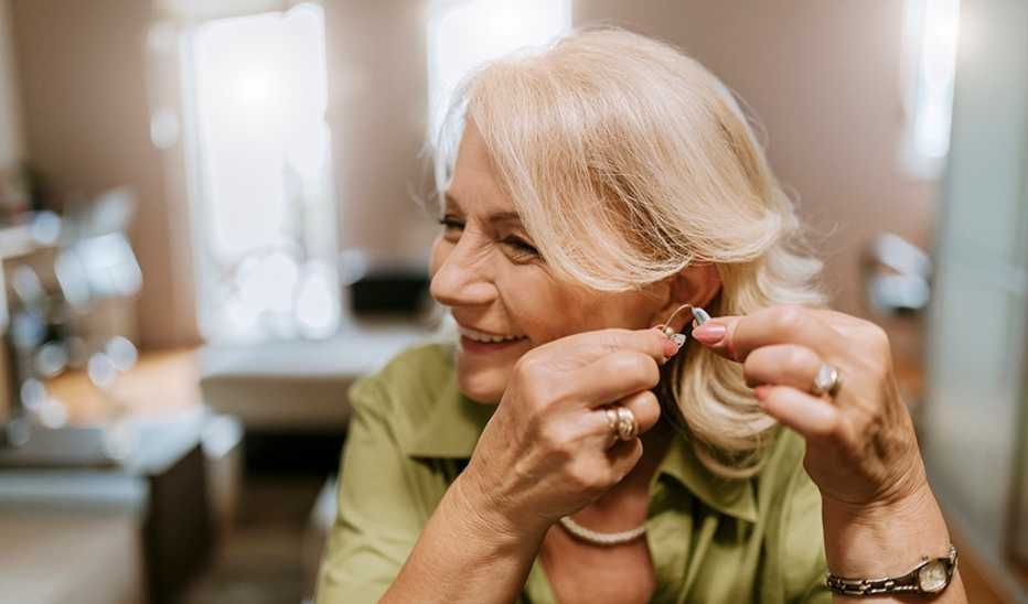 A smiling woman putting a hearing aid in her ear