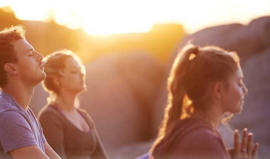 Three people meditating outside at sunset