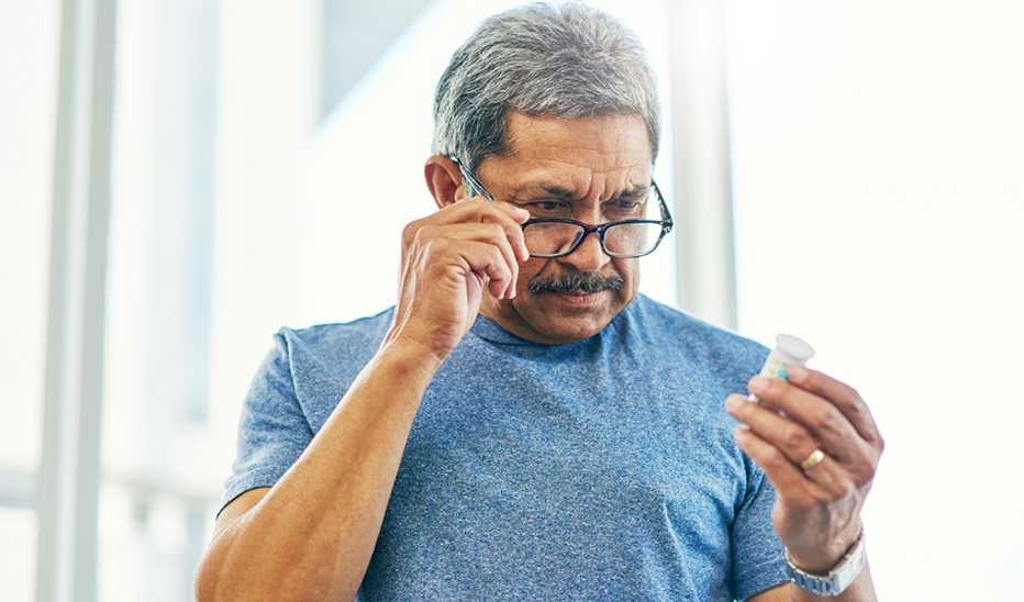 A man wearing reading glasses to check the label on a bottle of supplements