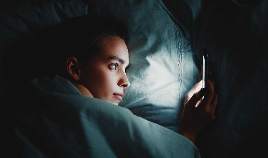A woman using phone while lying in bed in a dark room