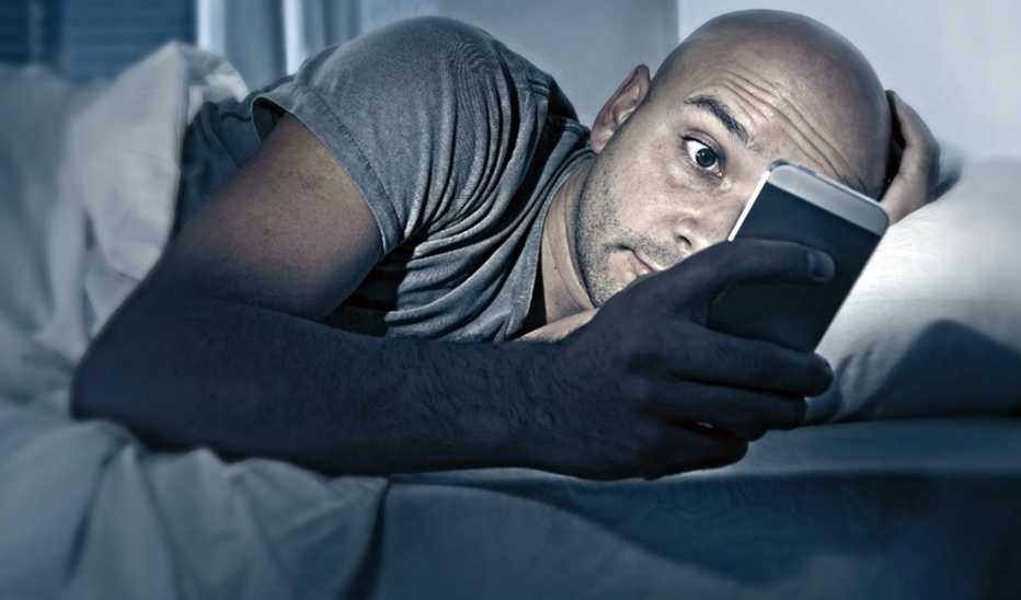 A man looking at his phone while in bed