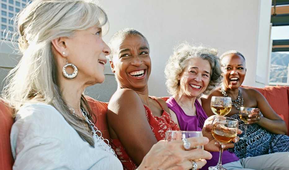 Four women drinking wine together on a couch on a rooftop