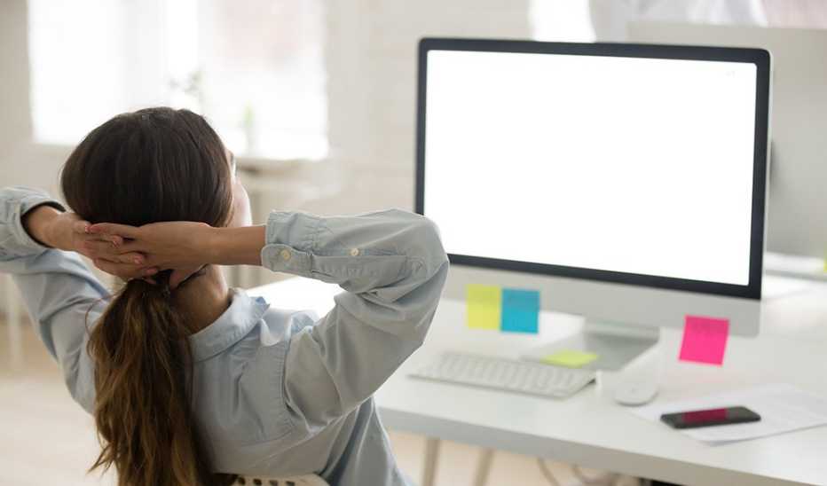 A woman leaning back in a chair in front of a computer with her hands behind her head