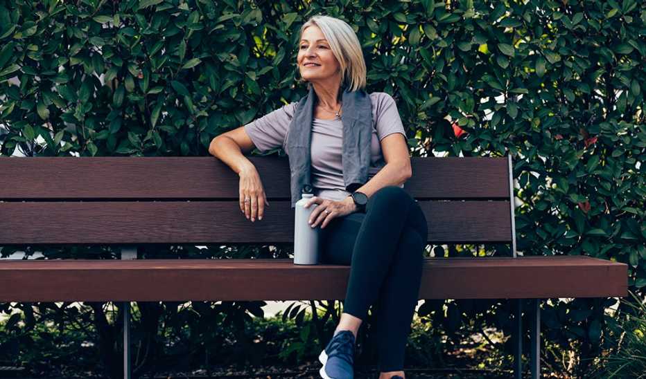 A woman sitting on a park bench with a water bottle in her hand