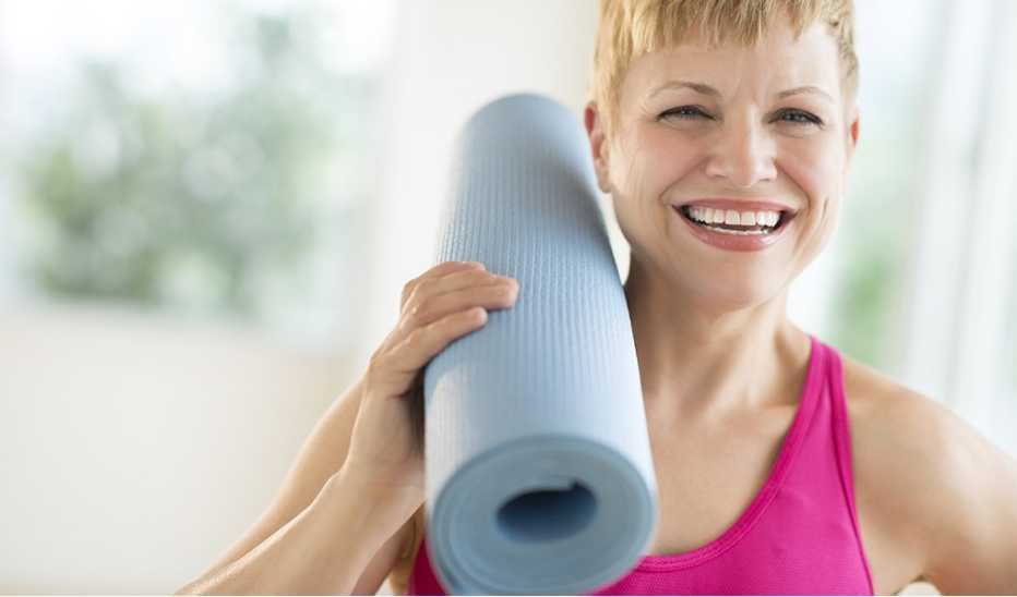 A woman holding a yoga mat on her shoulder