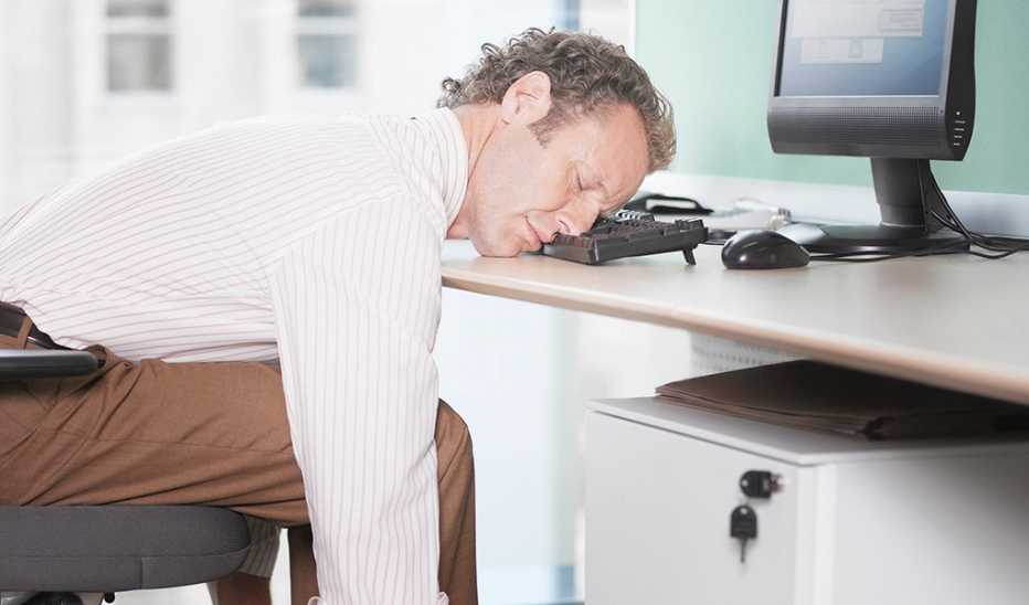 A man sleeping with his head on his computer keyboard