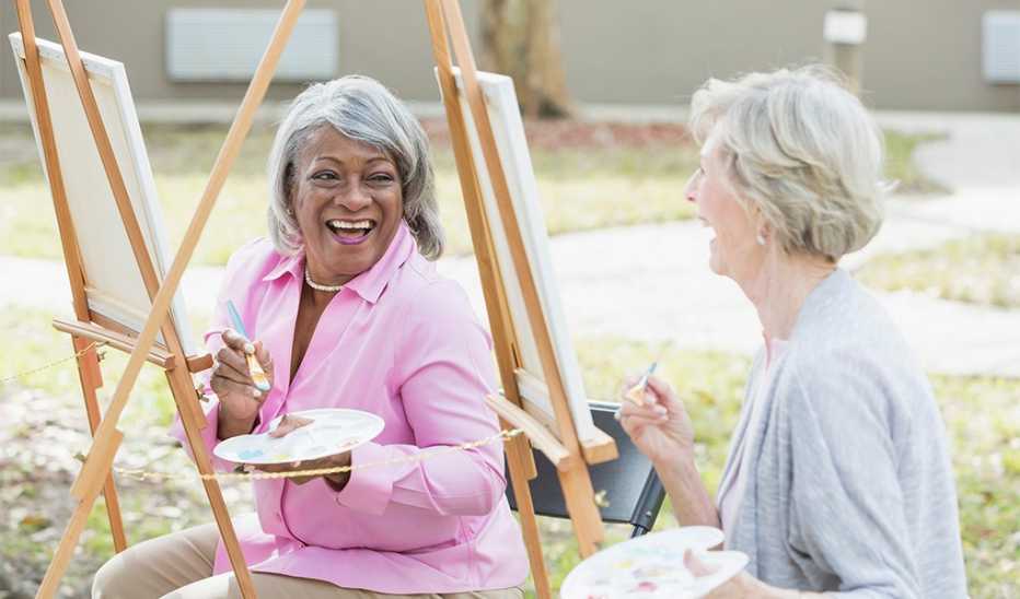 Two women smiling and laughing as they paint outdoors