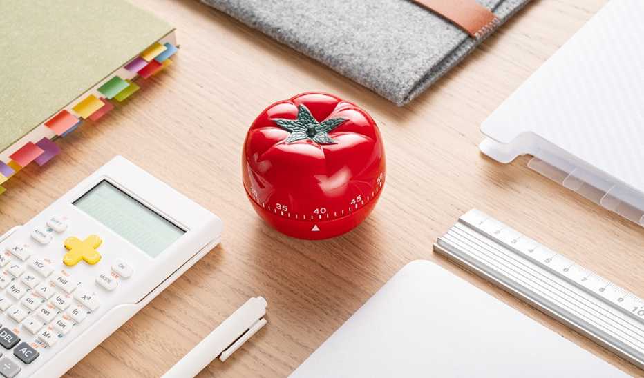 A close-up view of a red tomato timer on a wooden desk