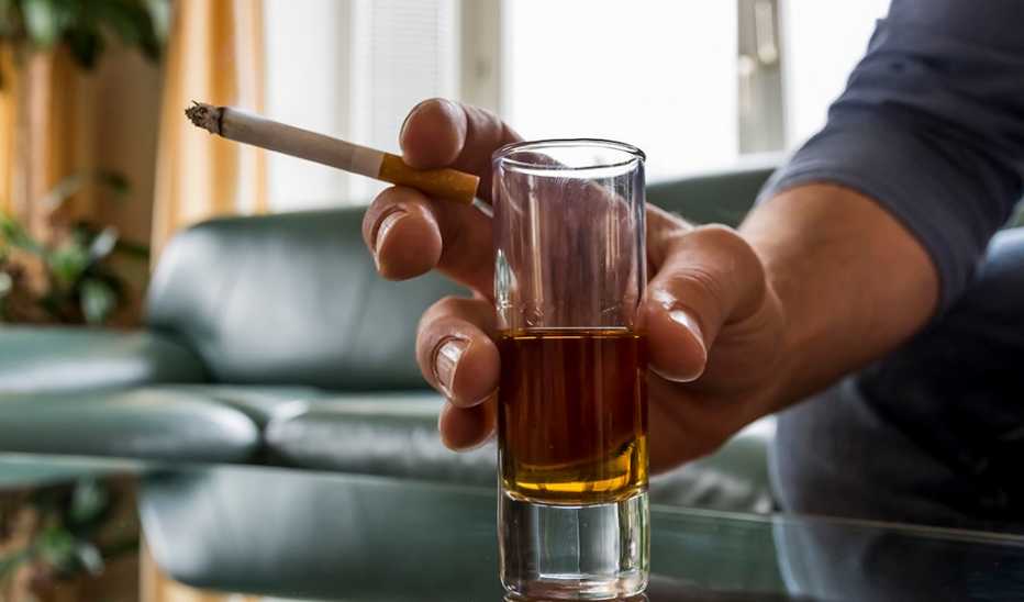 A close up of a hand holding a cigarette and shot glass
