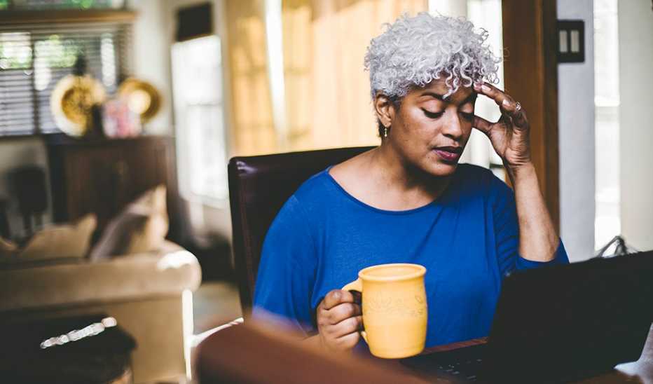 A woman appearing stressed while working on laptop on a table at home