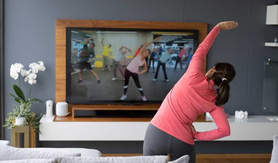 Back view of a woman stretching as she watches an exercise class on TV