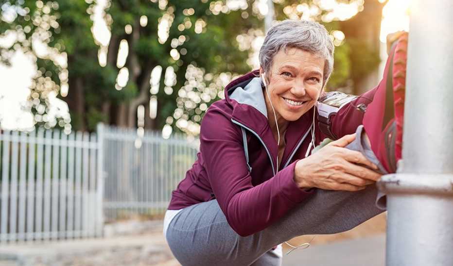 A smiling woman stretching her leg on a pole before going on a run