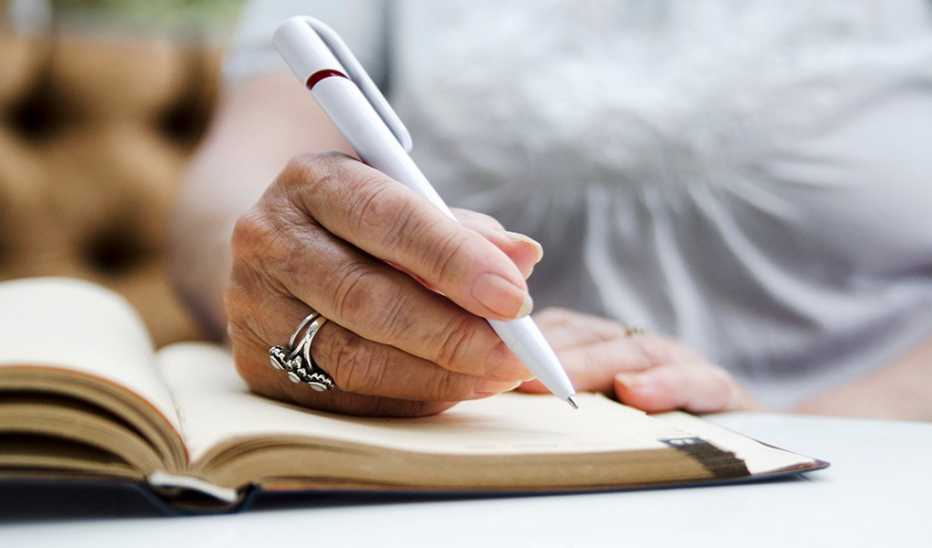 A close up of a hand writing with a pen in a journal