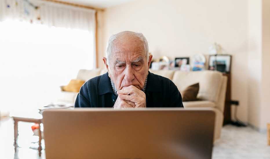 A man with his hands on his chin in front of a laptop at home