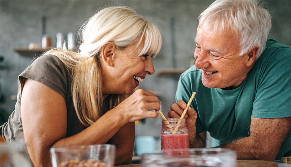 A man and woman drinking a smoothie together in a kitchen