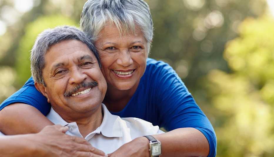 A smiling woman hugging a smiling man from behind while outside