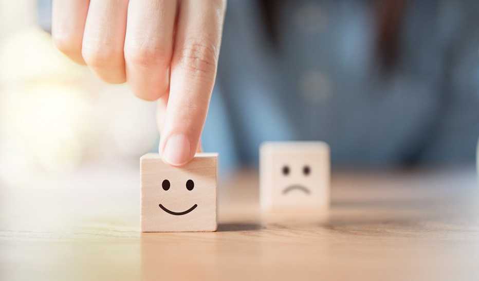 Close up of a hand touching a wooden cube with a smiley face on it
