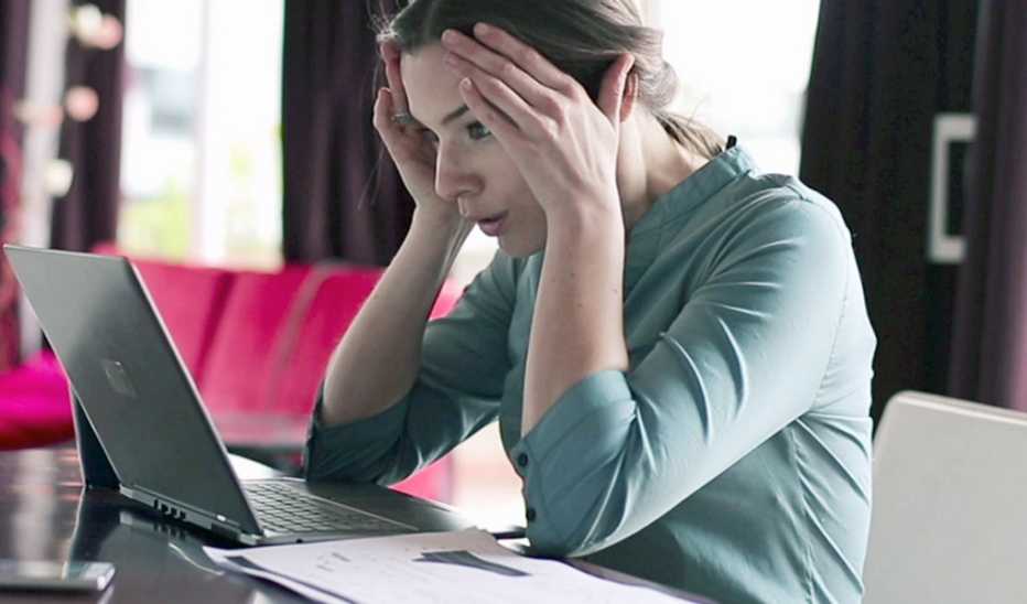 A woman holding her hands to her head while using a laptop
