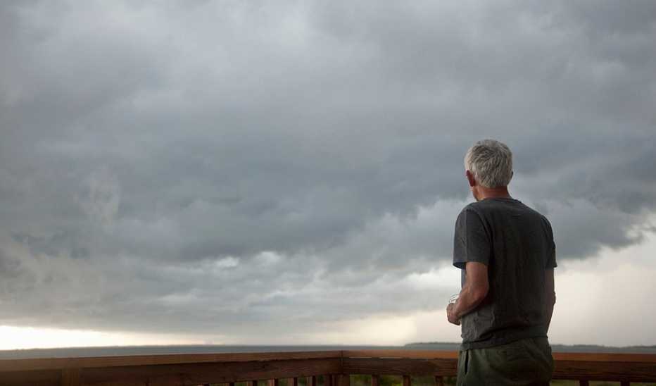 A rear view of a man staring out at stormy skies