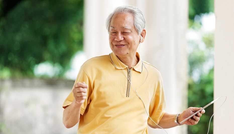 A man with earbuds in his ears listening and dancing to music with a tablet in his hand