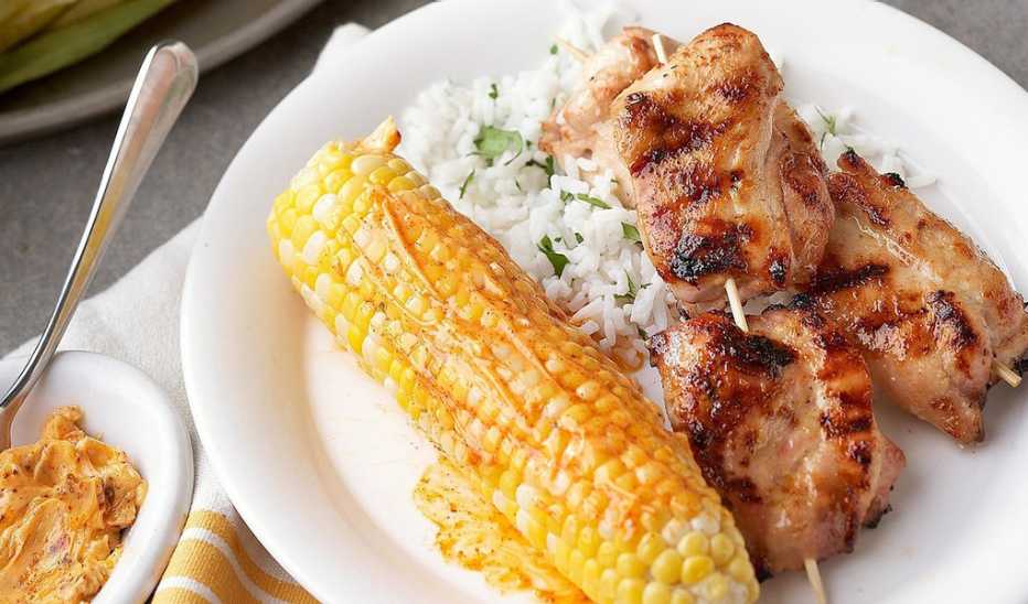 A close-up view of a chicken churrascada with grilled corn and paprika butter on a plate