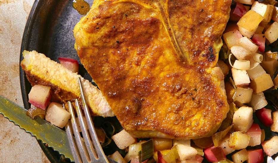 A close-up view of curried pork chops with apples and leeks in a pan
