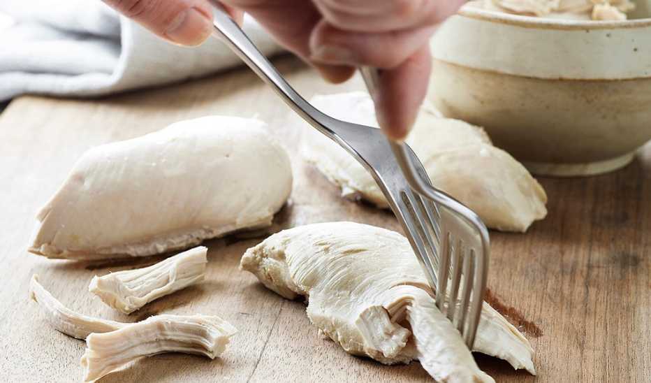 A close-up view of poached chicken with forks in it A close-up view of poached chicken with forks in it