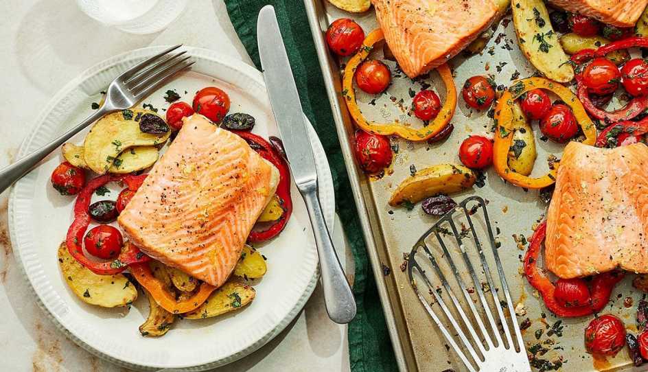 A close-up view of sheet-pan roasted salmon and vegetables on a plate and pan