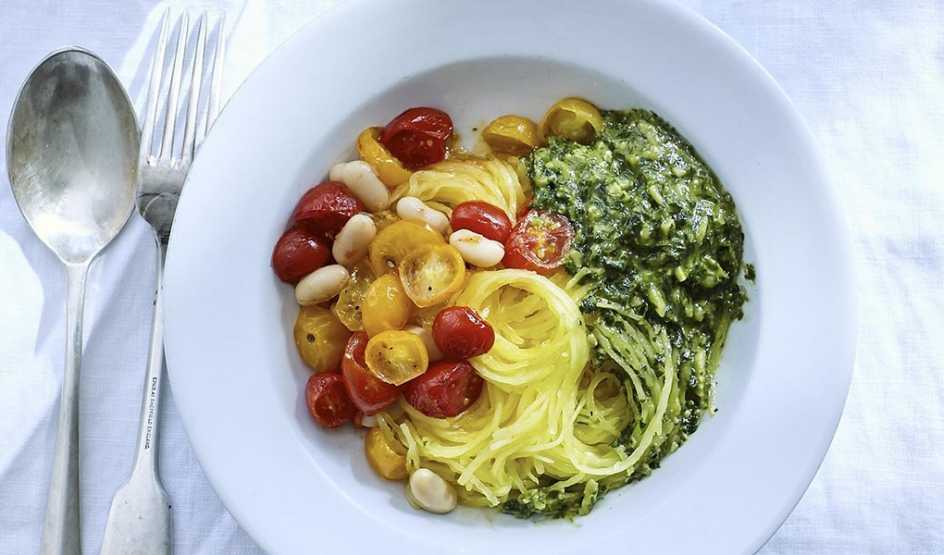 A close-up view of spaghetti squash with roasted tomatoes, beans and almond pesto in a bowl