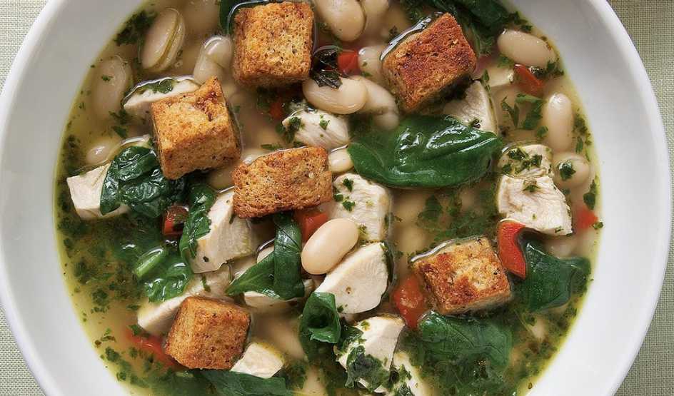 A close-up view of a chicken and spinach soup with fresh pesto in a bowl