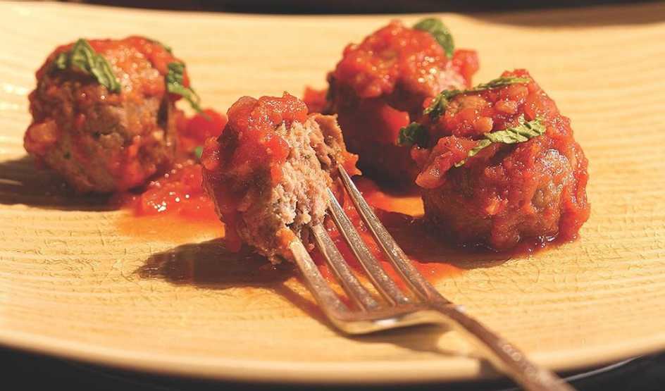 A close-up view of spicy lamb meatballs in tomato sauce on a plate