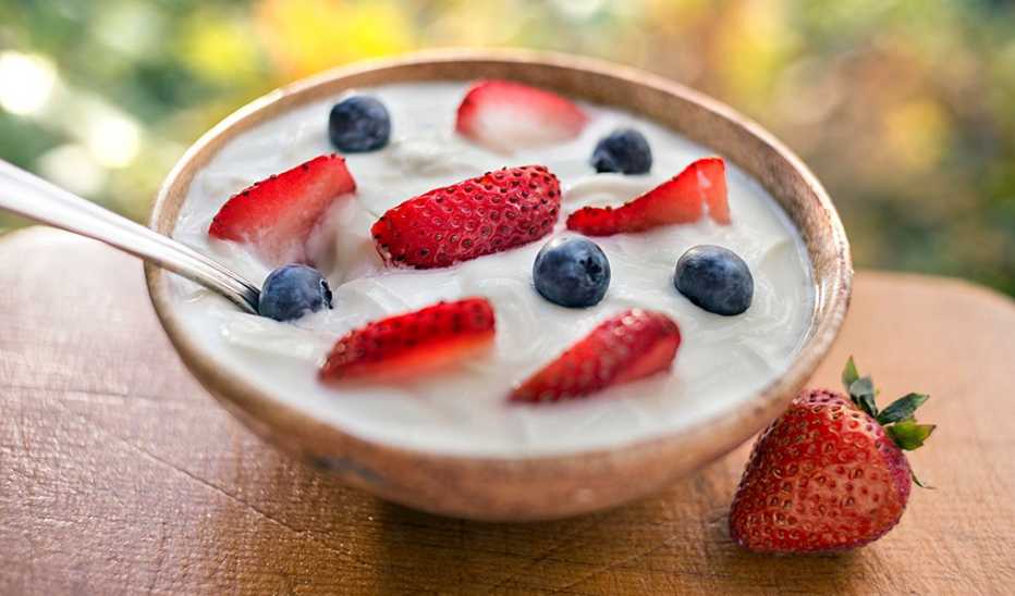 A close-up view of a bowl of yogurt with strawberries and blueberries in it